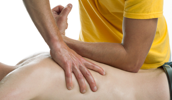 Ein Physiotherapeut massiert den Ruecken des Patienten mit seinem Unterarm.