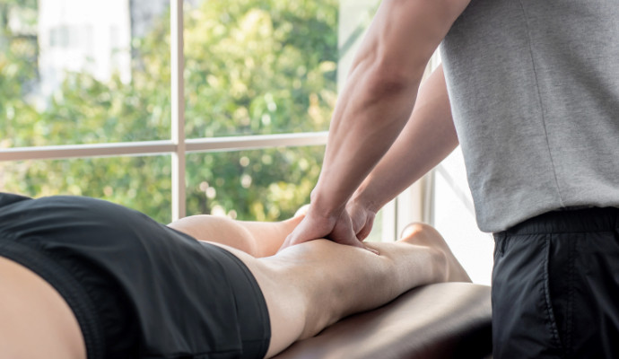 Ein Physiotherapeut massiert die Waden eines Mannes um die Muskeln zu entspannen.